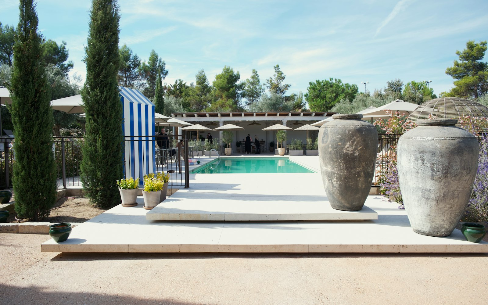 Bassin bordé de cyprès et de jarres en terre cuite sur une terrasse en pierre claire