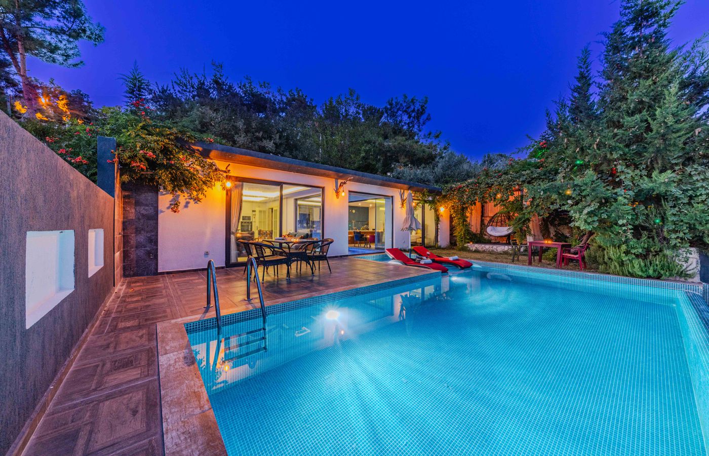 Villa moderne au crépuscule, piscine éclairée bordée de végétation