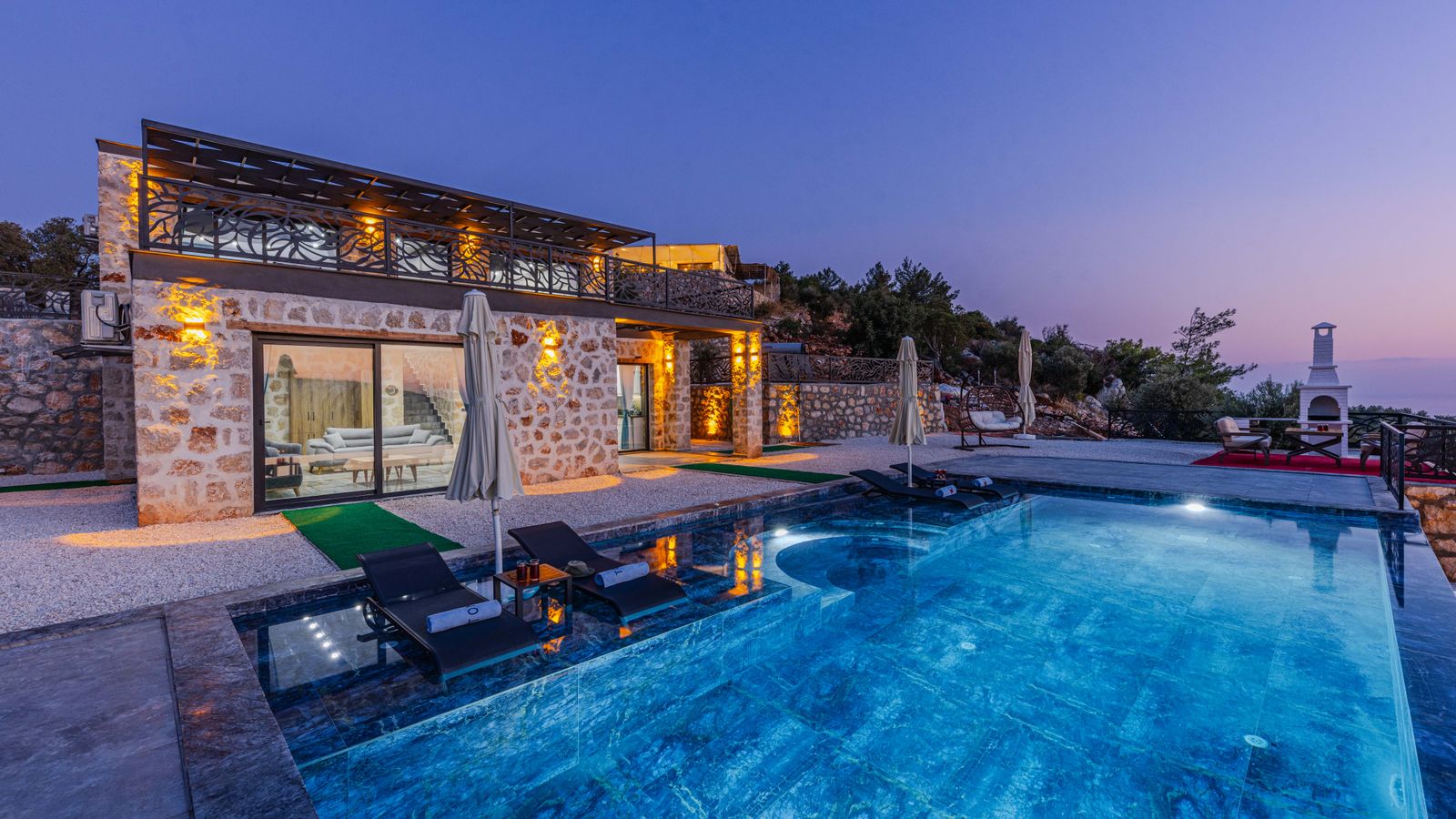 Villa en pierre éclairée au crépuscule, sa piscine bleue au premier plan