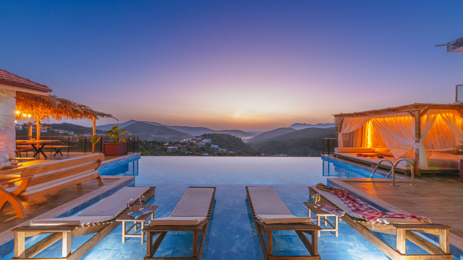 Piscine à débordement face aux collines au coucher du soleil, transats alignés