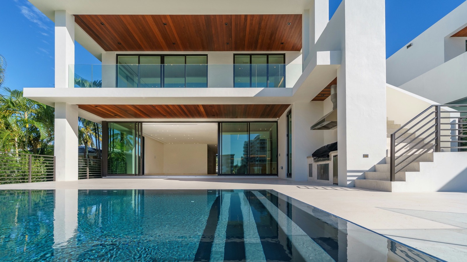 Villa contemporaine blanche aux plafonds de bois, reflétée dans la piscine au premier plan