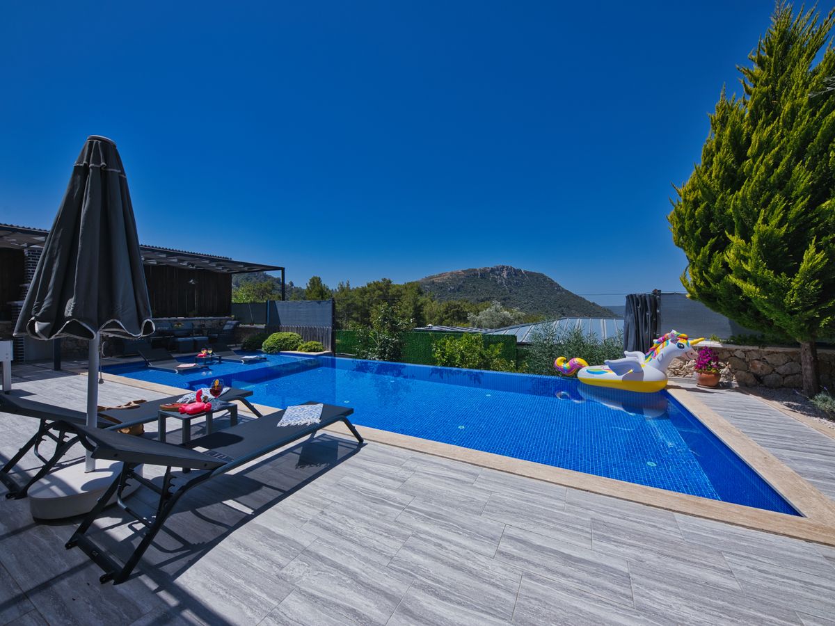 Piscine bordée de transats et d’un parasol, montagnes à l’horizon