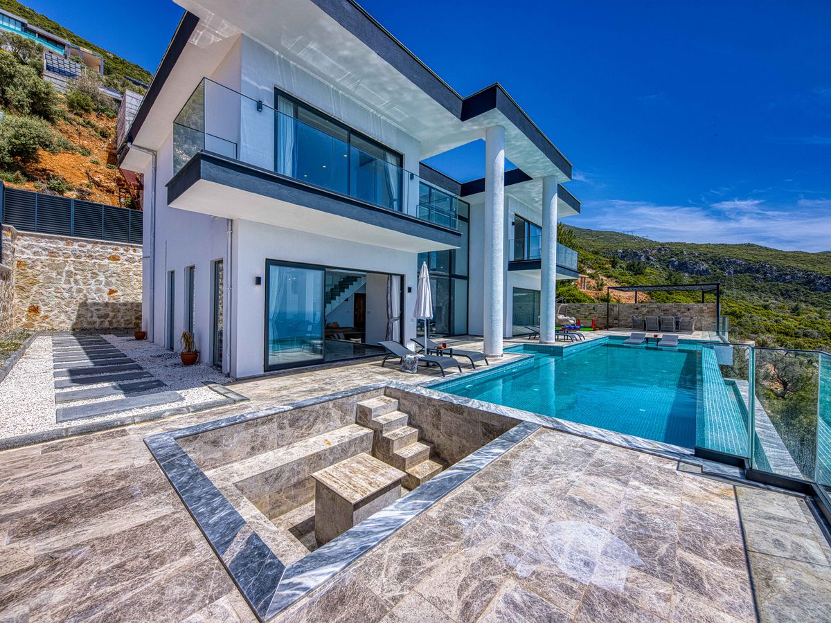 Piscine à débordement longeant une villa de verre et de pierre